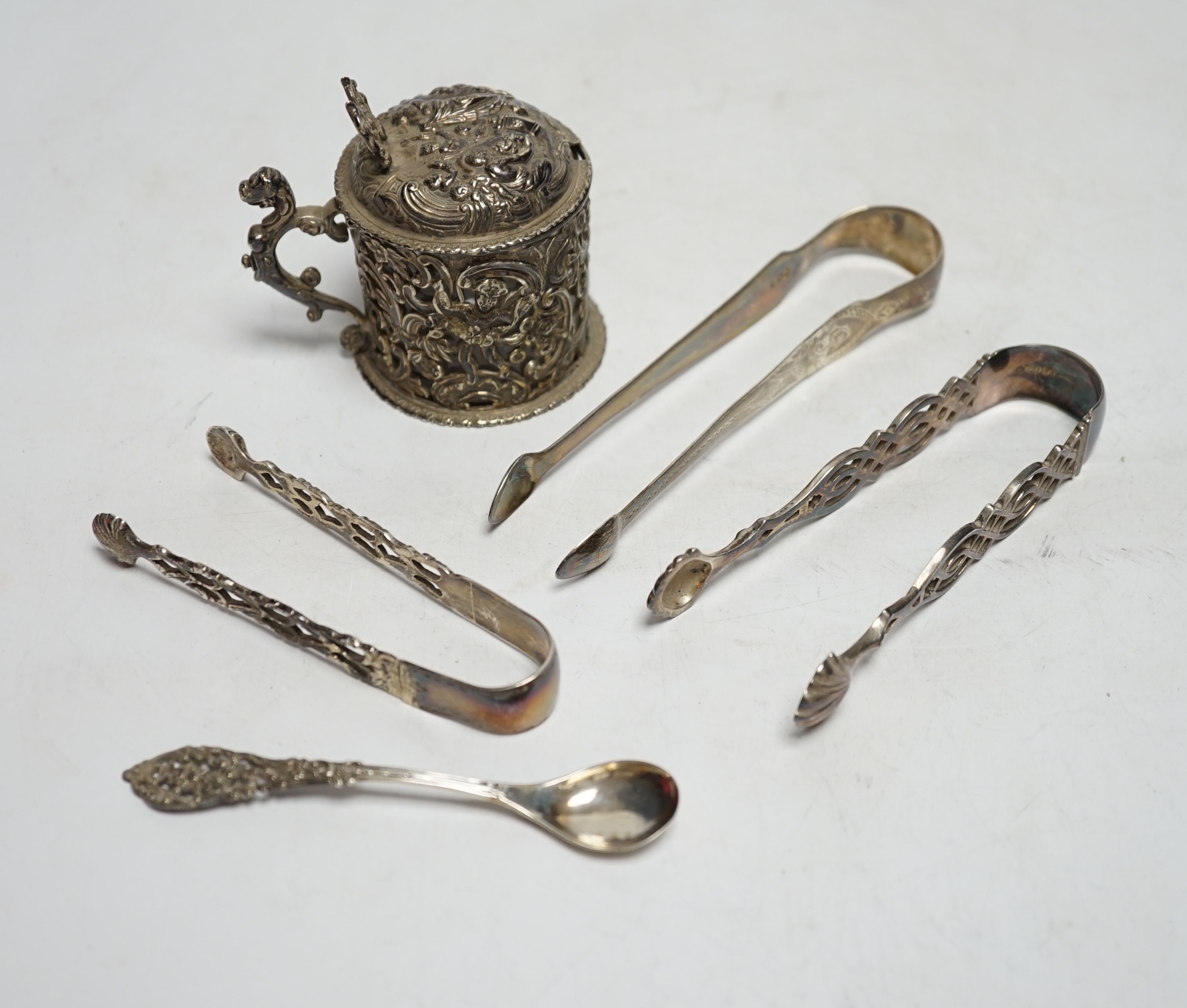 A Victorian silver embossed mustard pot, with spoon and three pairs of George III and later silver sugar tongs.